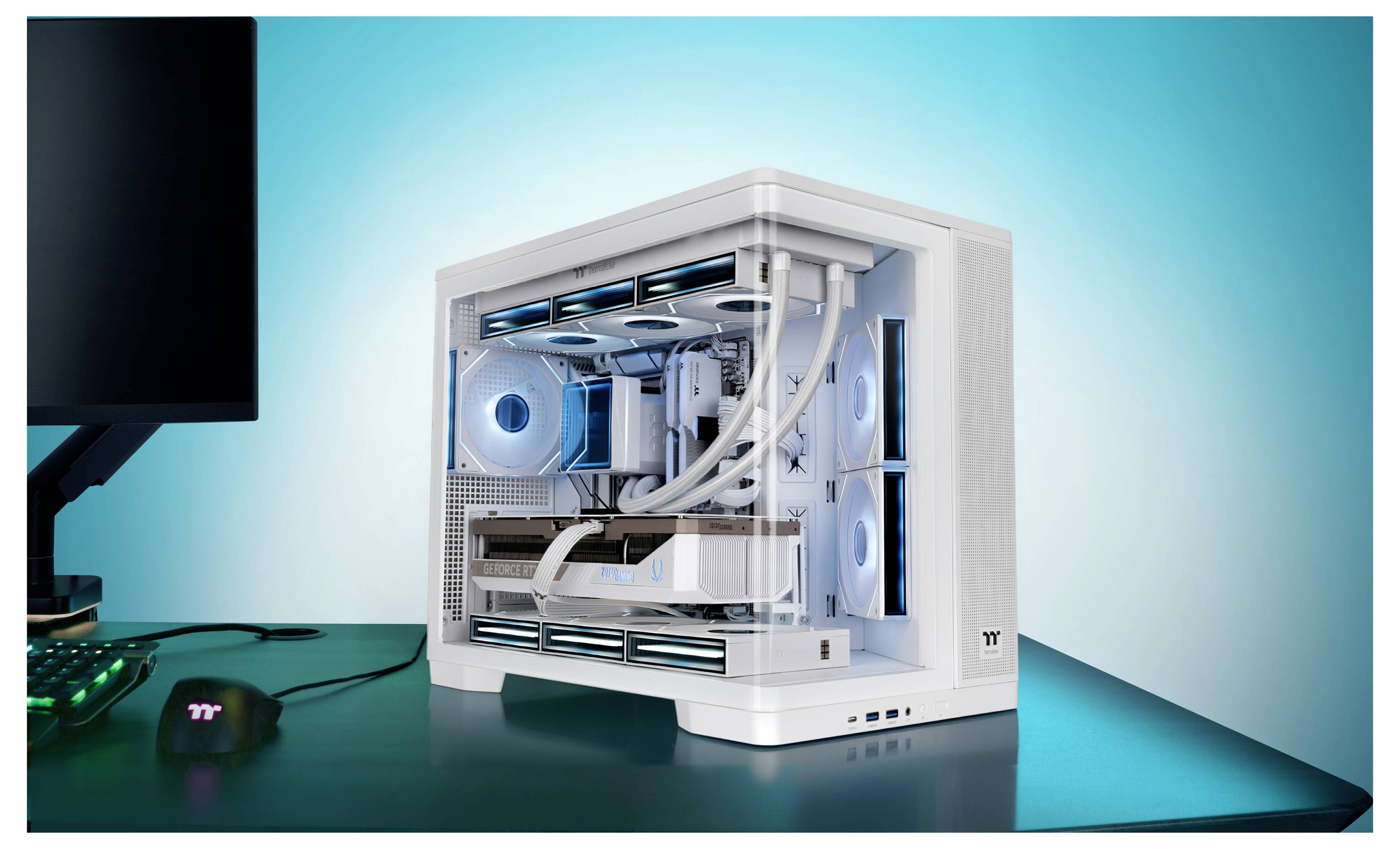 Tour de jeu de bureau blanc avec le panneau latéral retiré, montrant les ventilateurs de refroidissement illuminés en bleu et les composants internes sur un bureau à côté d'un moniteur et une souris.