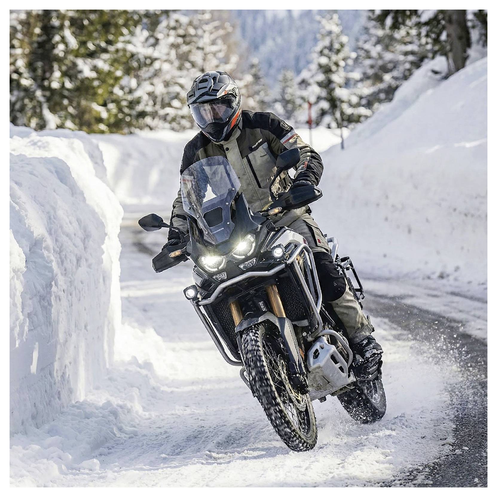 Motocycliste roulant sur un vélo tout-terrain à travers un sentier de montagne enneigé, s'inclinant dans un virage avec les phares allumés.