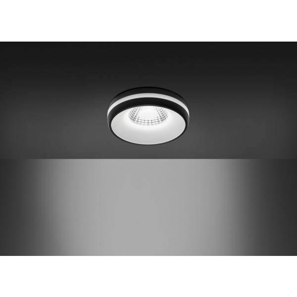 Luminaire LED rond suspendu au plafond avec monture noire, illuminant un mur gris.