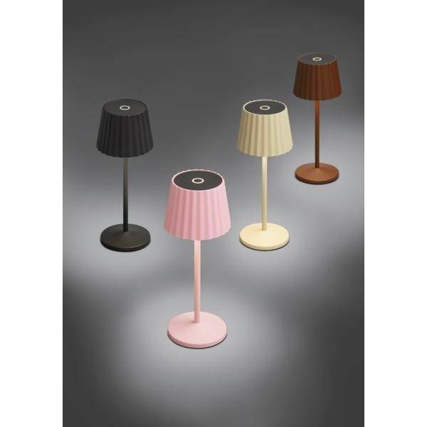 Quatre petites lampes de table sans fil en noir, rose, crème et marron, chacune avec un abat-jour plissé et une base ronde sur un fond gris.