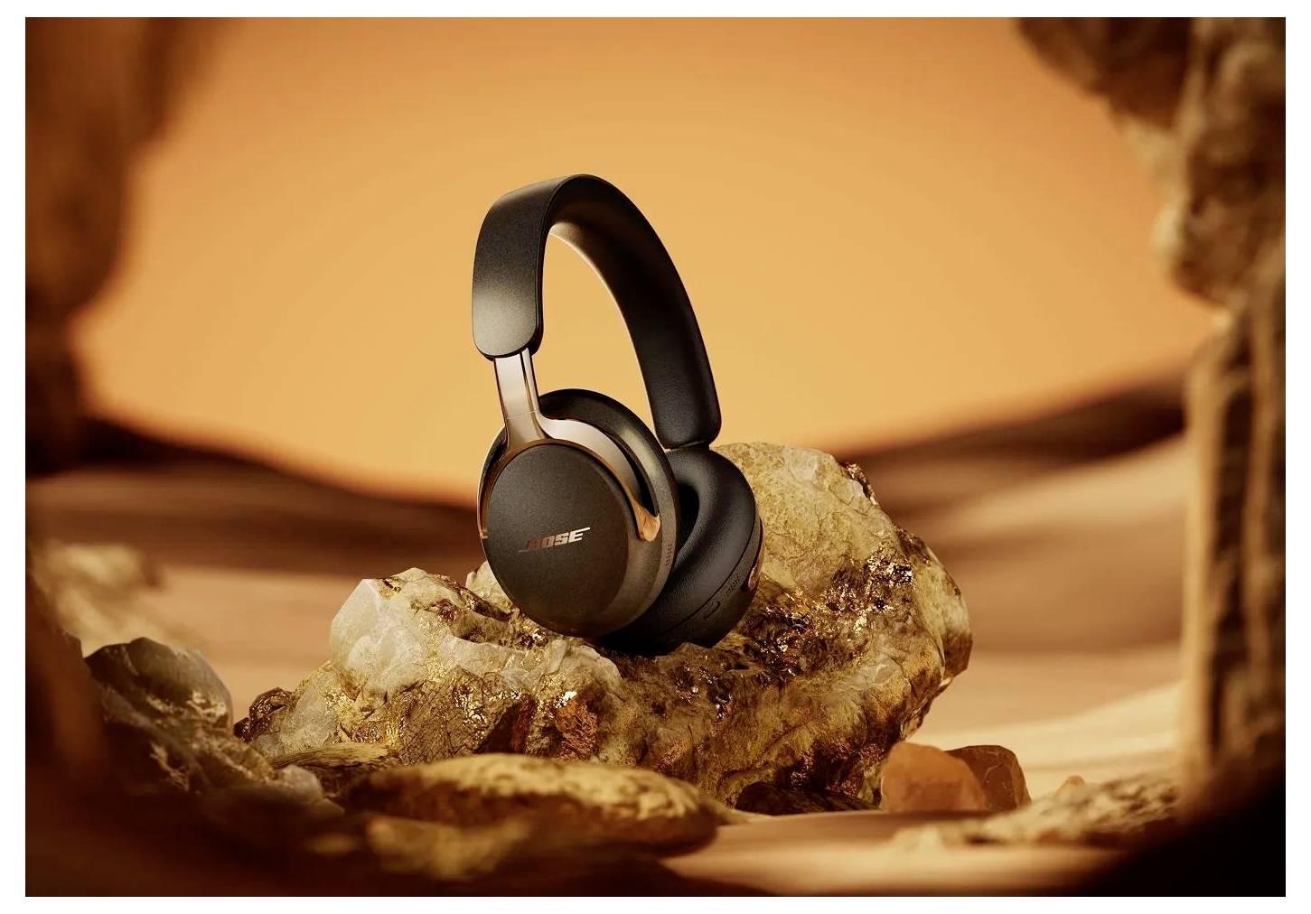 Des écouteurs Bose supra-auriculaires noirs reposant sur un rocher dans un cadre désertique chaud aux tons orangés.