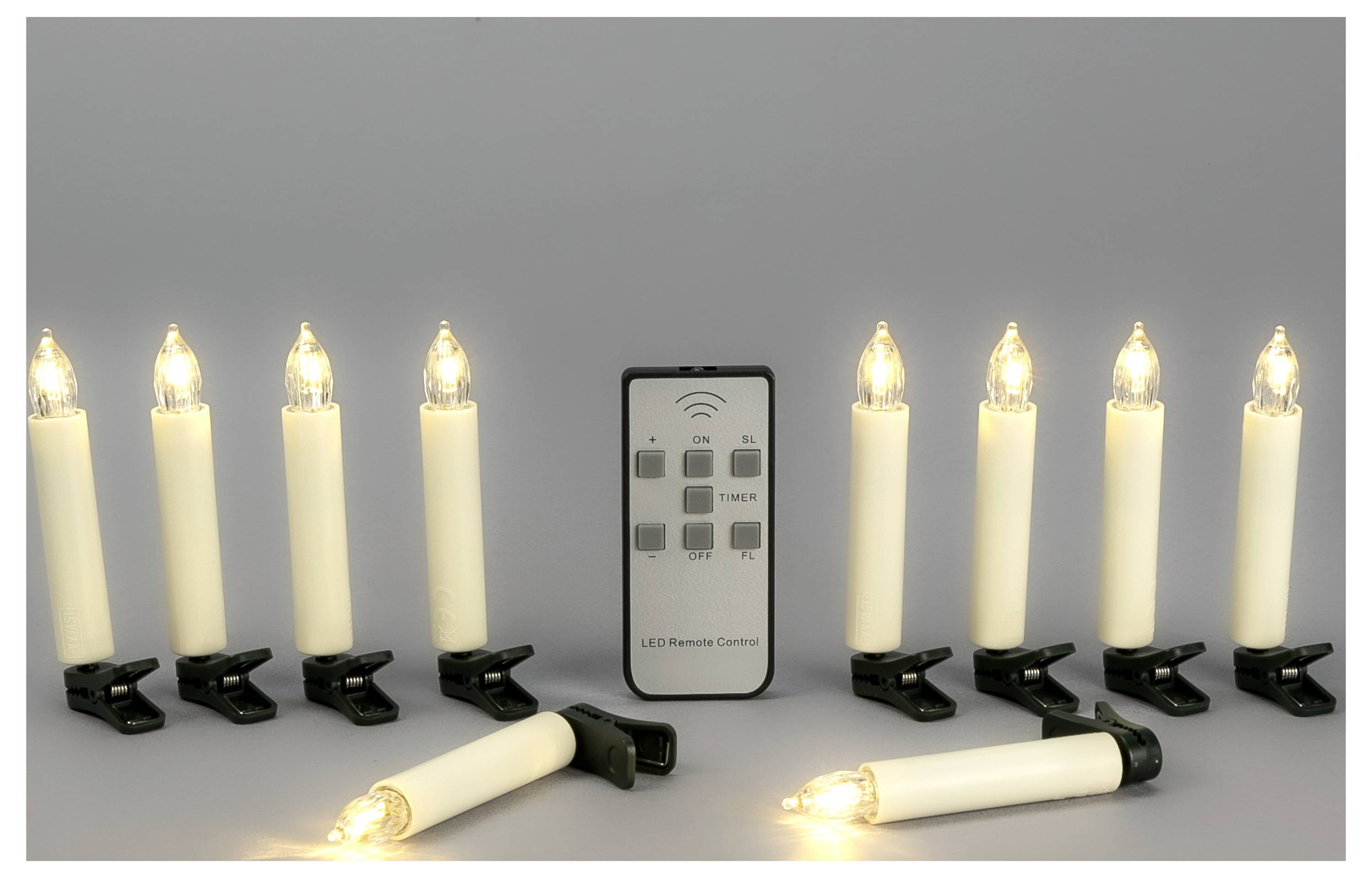 Ensemble de huit bougies LED sans flamme avec télécommande, deux bougies allumées couchées devant et les autres debout sur des pinces sur un fond gris.