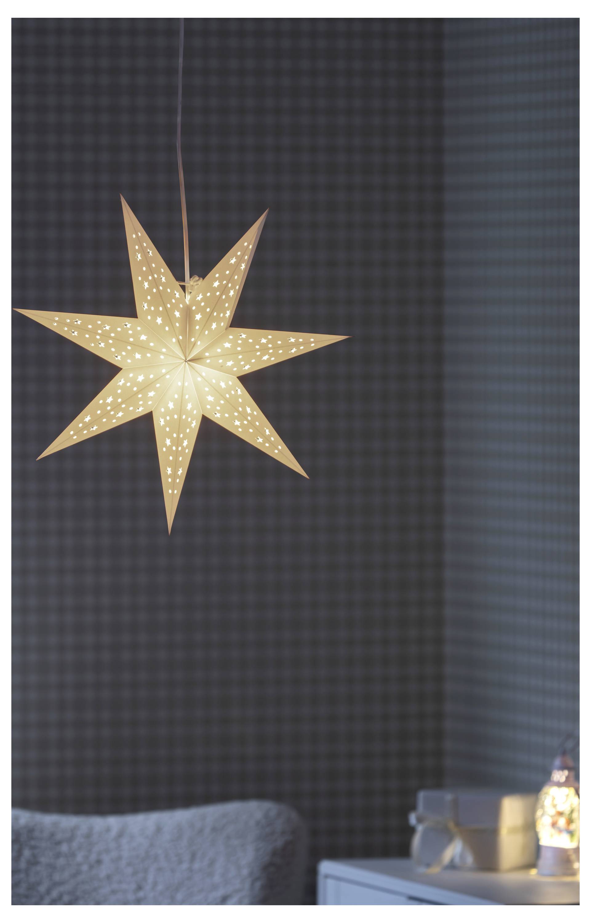 Un luminaire pendentif en forme d'étoile à huit points brillante pend au-dessus d'une pièce confortable avec un canapé et une petite lampe de table.