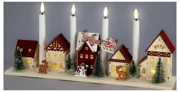 Une rangée de petites maisons de village de Noël illuminées avec des bougies allumées derrière elles, décorées de petits arbres miniatures et de figurines de fêtes sur une étagère.