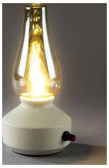 Lampe à huile allumée avec une cheminée en verre sur une base beige, présentée sur un fond gris uni.