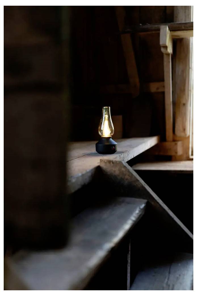 Une petite lanterne allumée repose sur une marche en bois dans un intérieur rustique tamisé.