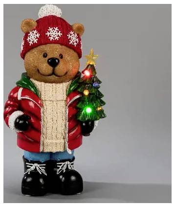 Figurine d'ours en peluche festive portant un bonnet d'hiver rouge et un manteau, tenant un sapin de Noël illuminé sur un fond gris.