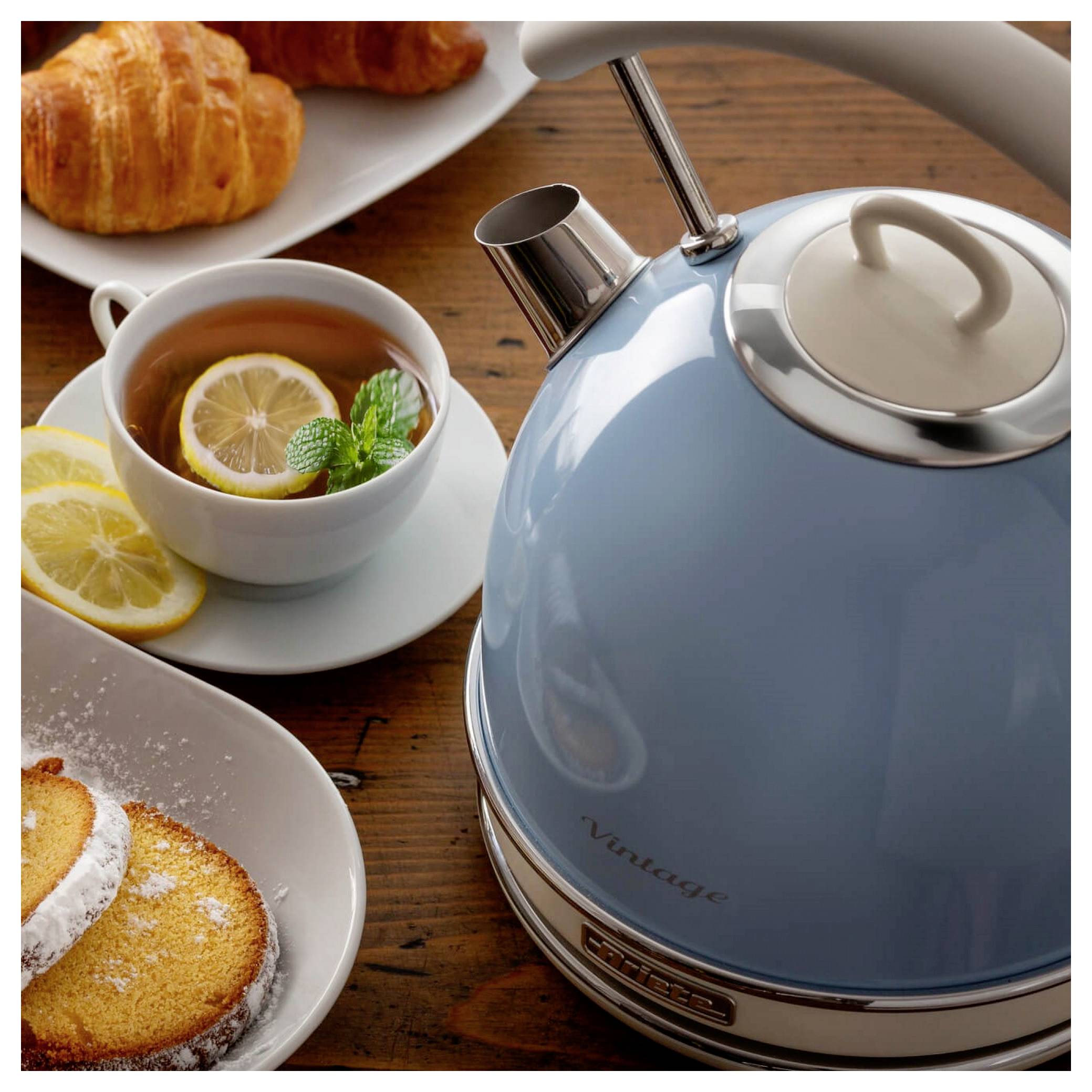 Bouilloire électrique bleue sur une table en bois à côté d'une tasse de thé au citron et de pâtisseries, évoquant un cadre de thé et petit-déjeuner.