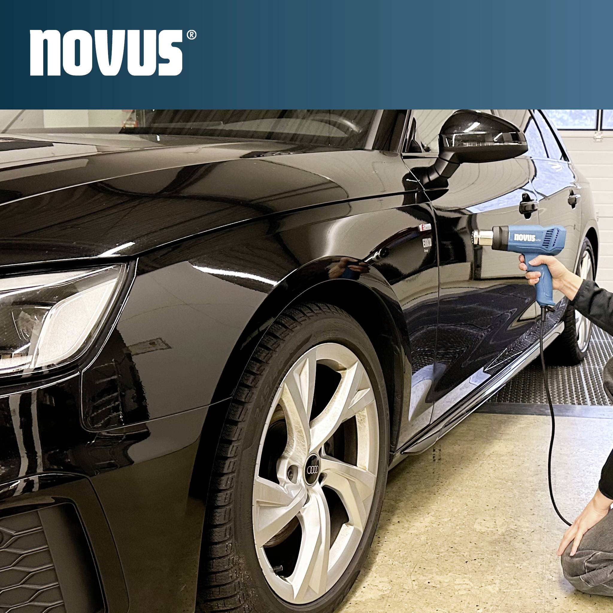 Une personne utilisant un pistolet thermique Novus pour réparer ou enlever des bosses sur le panneau latéral d'une voiture noire dans un garage.