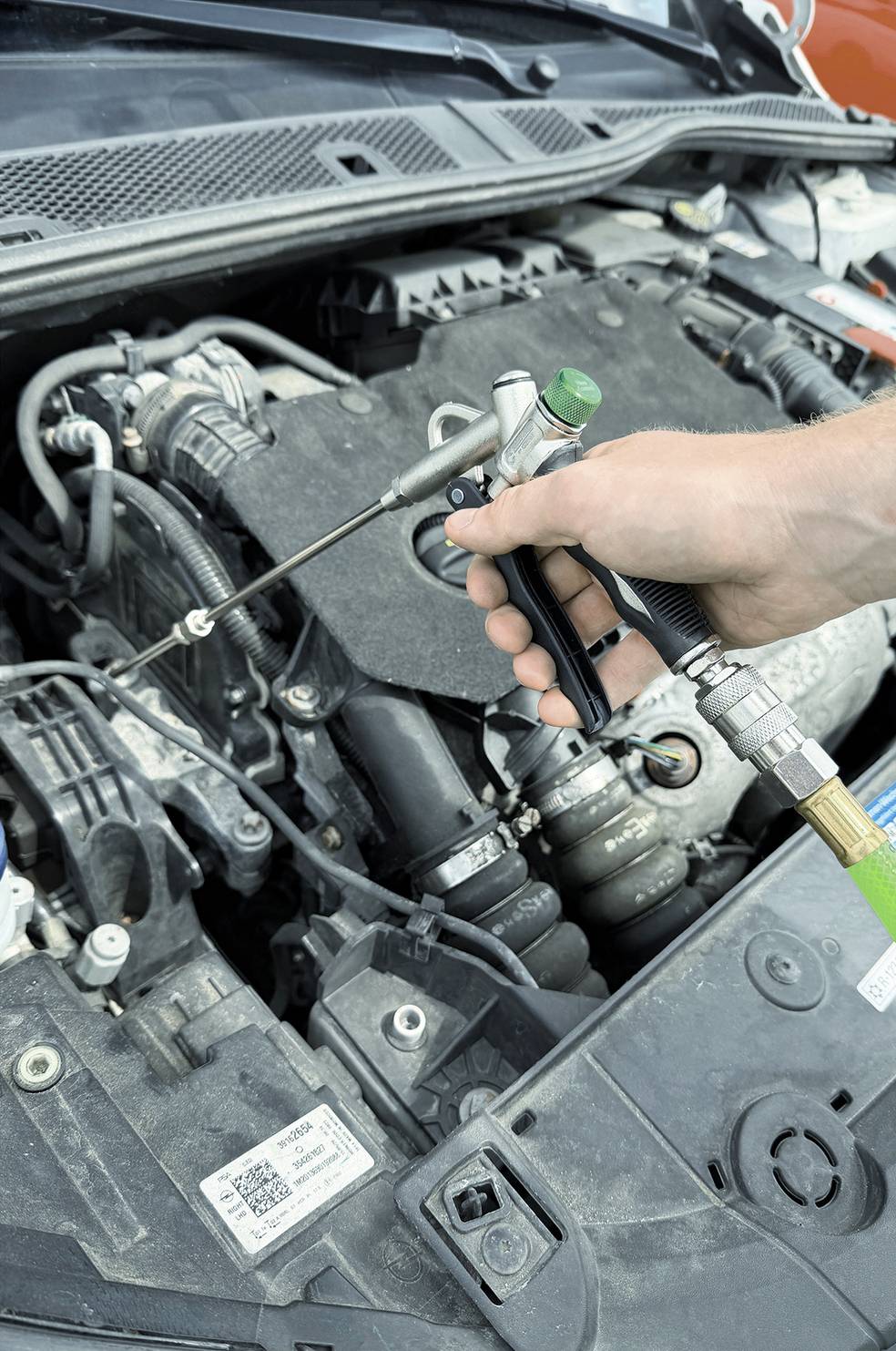 Un mécanicien utilisant un pistolet à air comprimé pour nettoyer le compartiment moteur d'une voiture sous le capot.