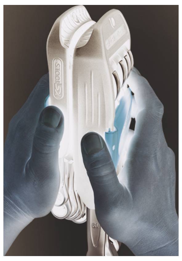 Des mains gantées de bleu tiennent un appareil ou un outil portatif en plastique blanc contre un fond sombre.