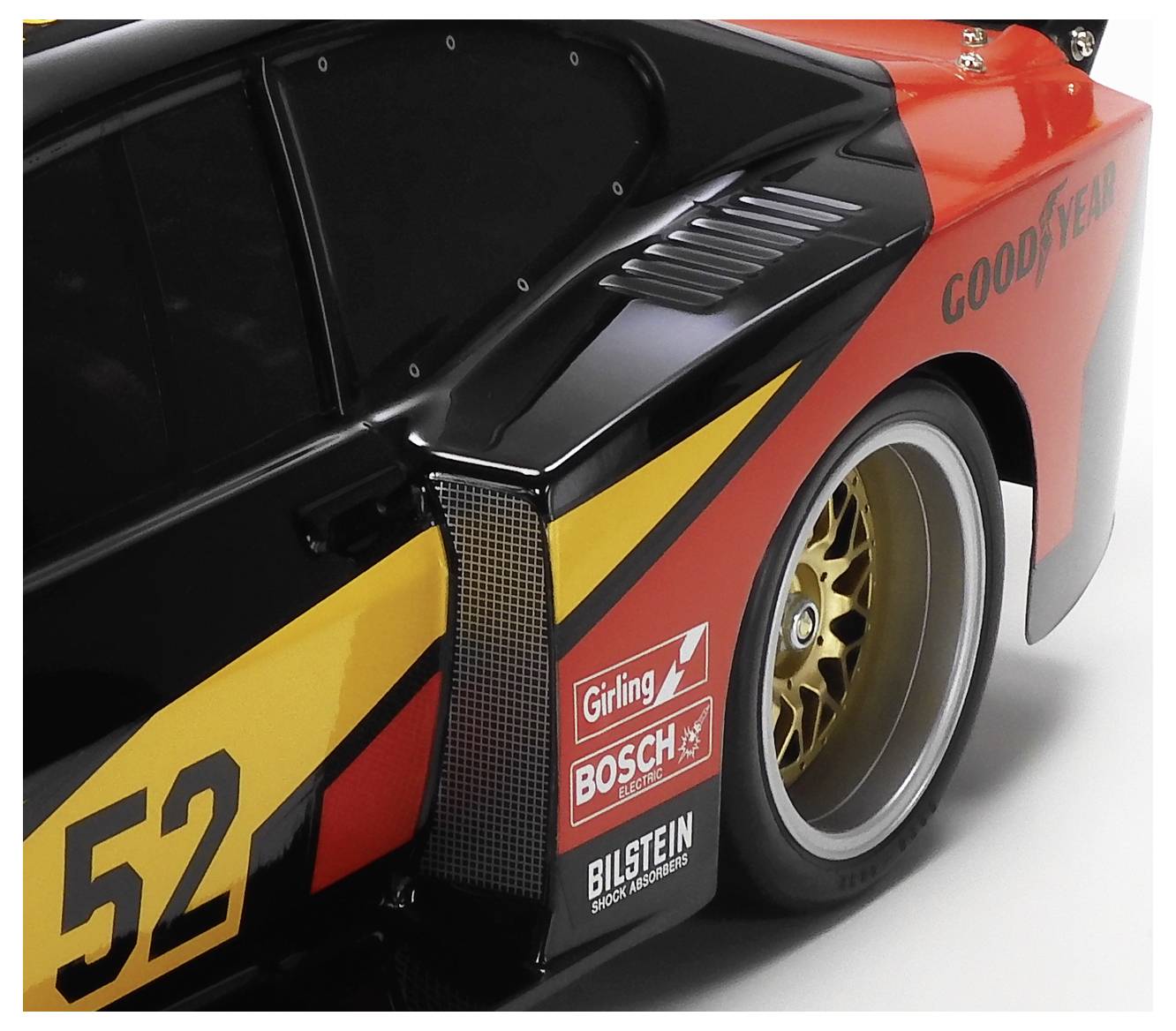 Gros plan du côté arrière d'une voiture de course, montrant le numéro 52, les décalcomanies de sponsors et la marque Goodyear sur une carrosserie noire, jaune et rouge.