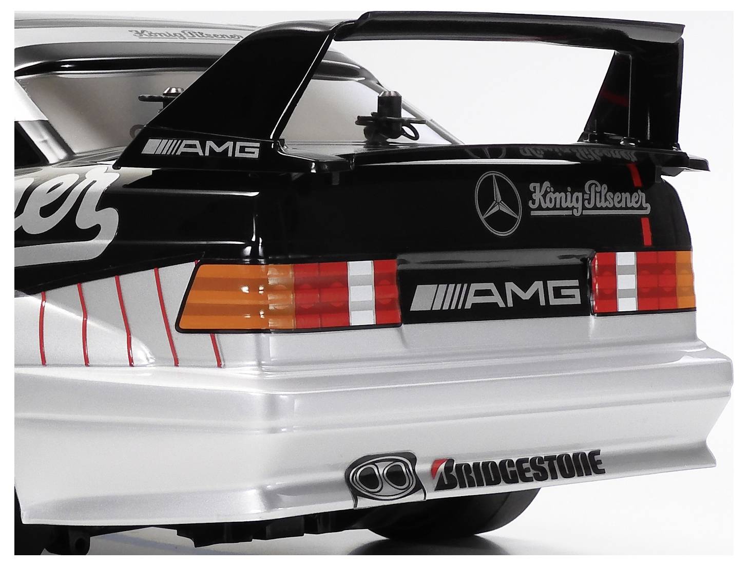 Vue arrière d'une maquette de voiture de course Mercedes AMG avec un grand aileron arrière, des logos de sponsors, et une livrée noire, argentée et rouge.