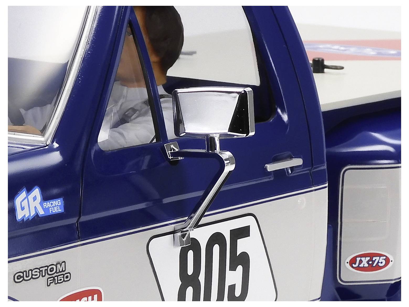 Camion de course bleu et blanc avec le numéro 805 et des autocollants de sponsors, vu de côté avec le conducteur visible à l'intérieur.