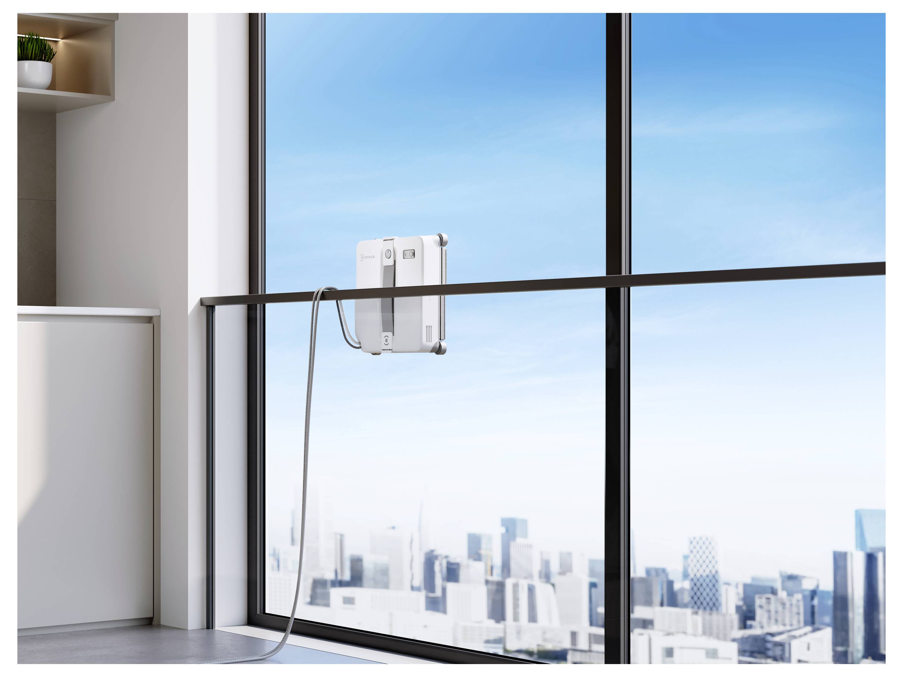 Robot nettoyeur de vitres monté sur une baie vitrée du sol au plafond, avec un cordon d'alimentation pendant au-dessus d'une skyline urbaine.