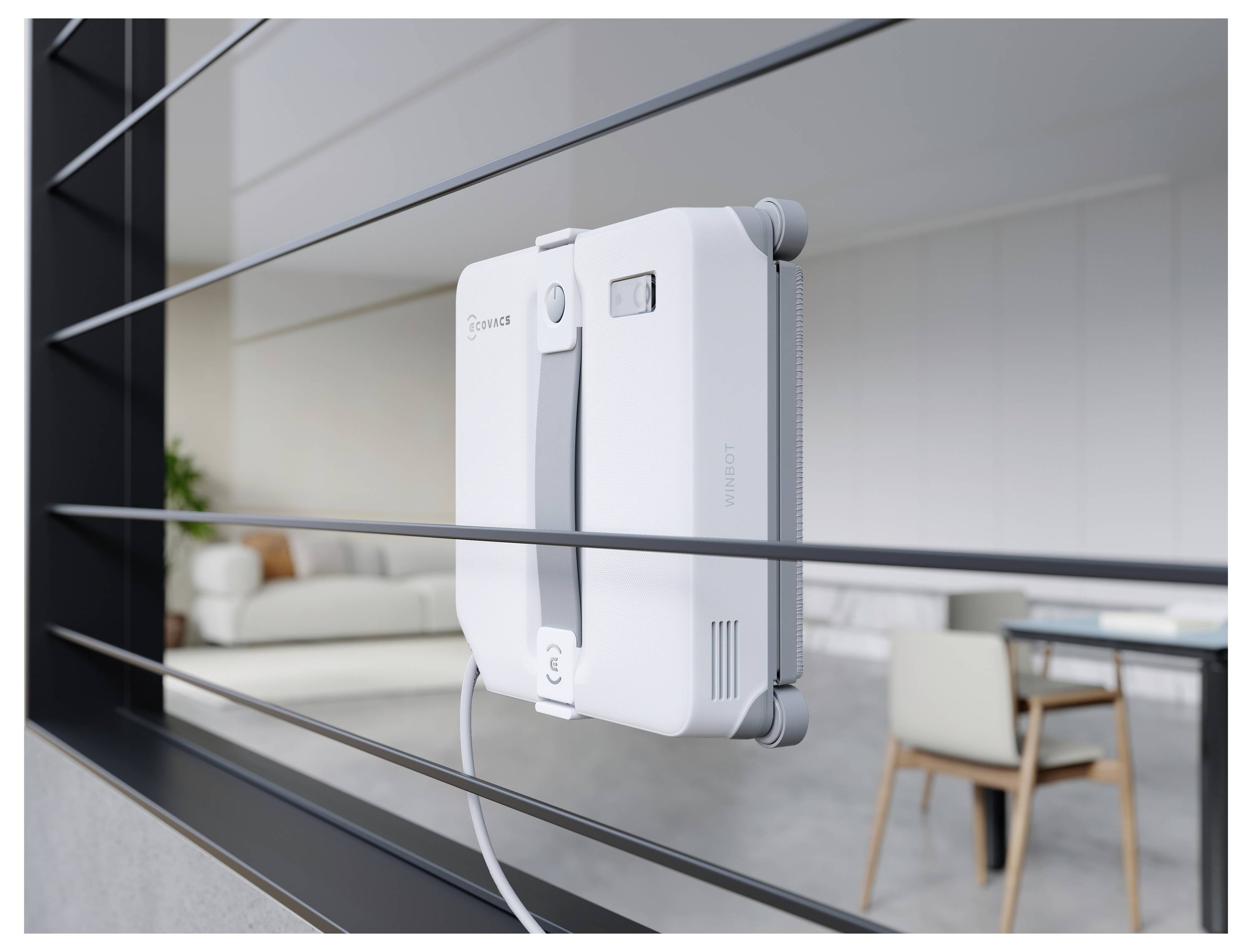 Un appareil de nettoyage de fenêtres robotique blanc est attaché à une vitre, avec un salon moderne visible derrière.
