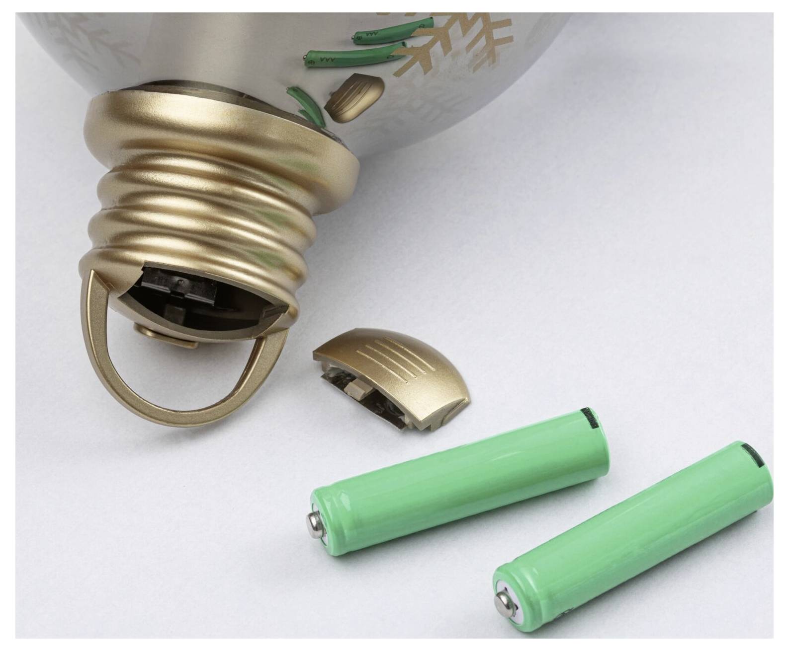 Une ampoule cassée avec deux piles vertes à côté sur un fond blanc, suggérant le recyclage ou le remplacement des piles.