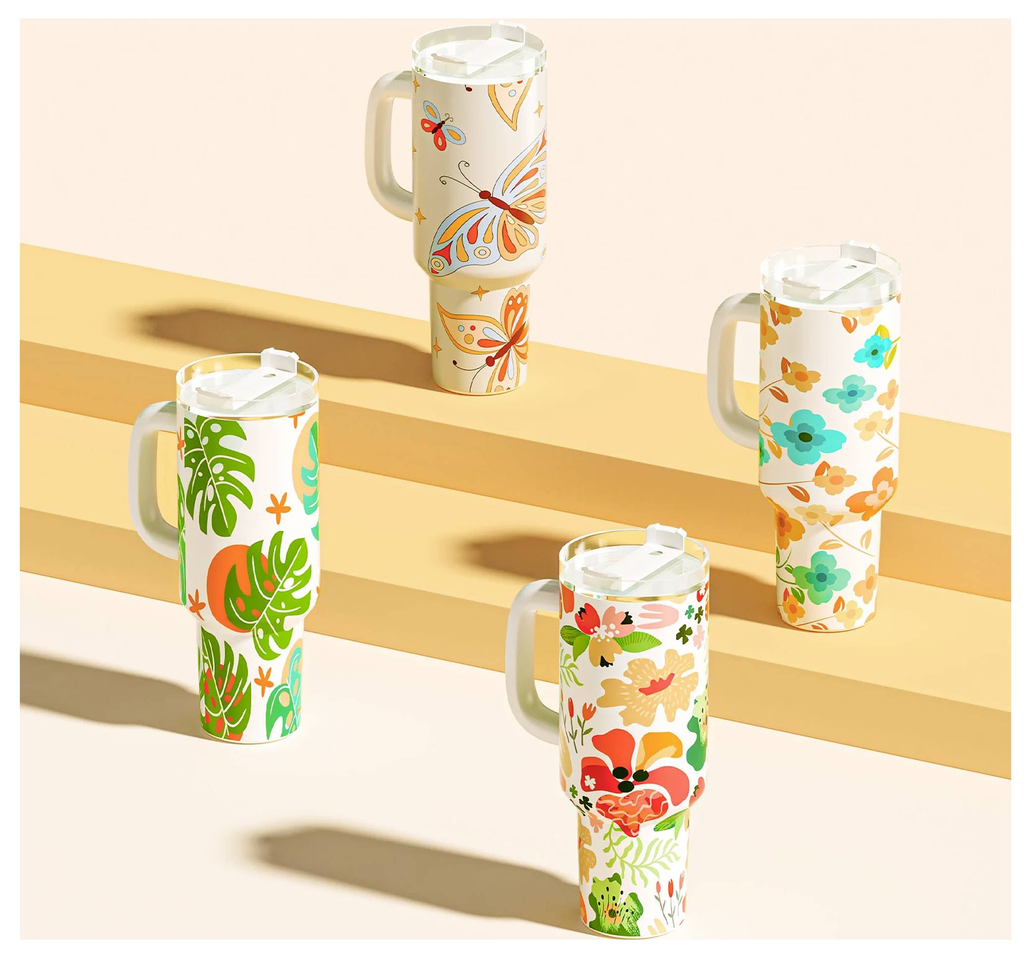 Quatre hauts gobelets à boire avec couvercles et poignées, chacun orné de motifs colorés de fleurs et de feuilles, disposés sur des surfaces étagées claires.