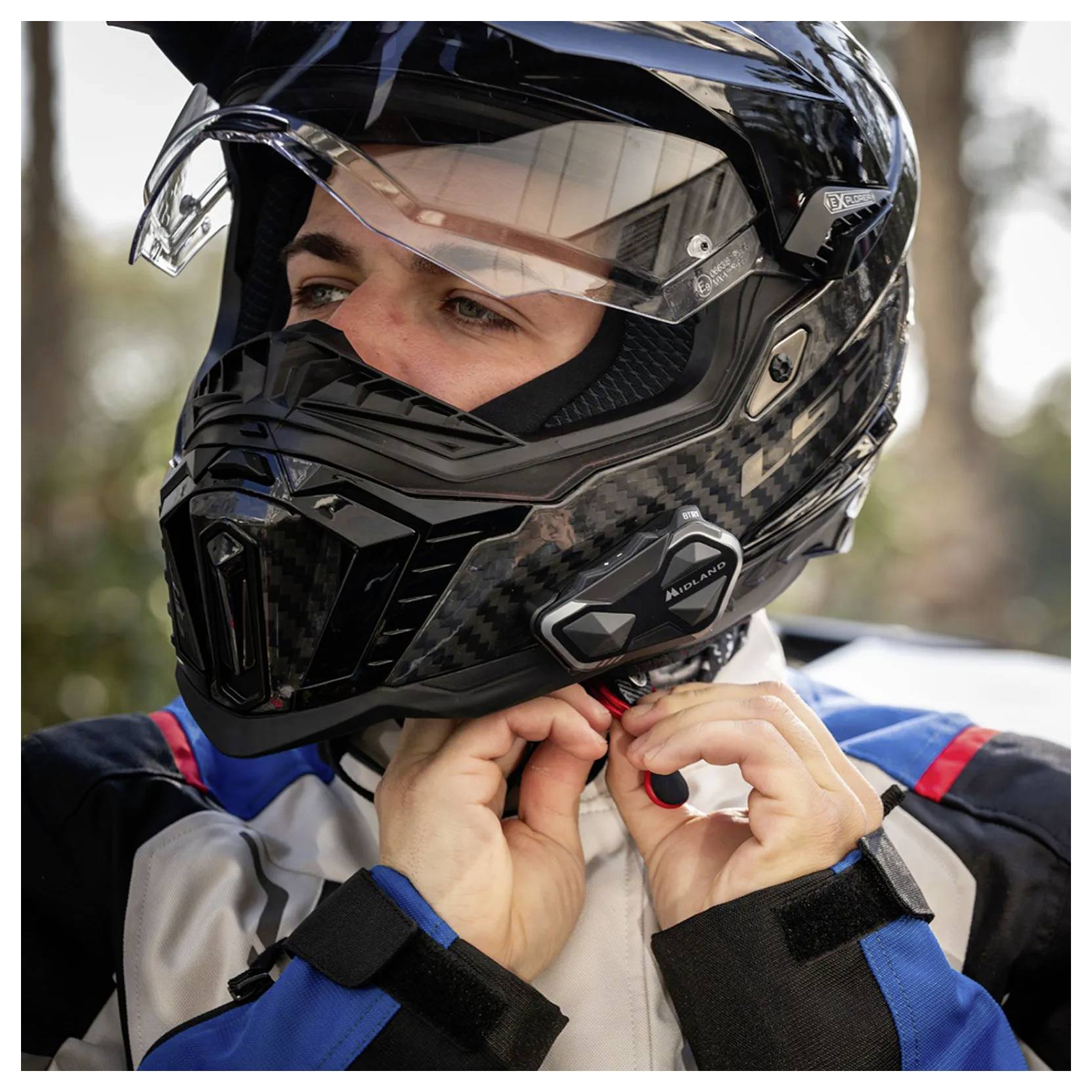 Personne portant un casque de moto intégral noir, attachant la jugulaire d'une combinaison de course à l'extérieur.