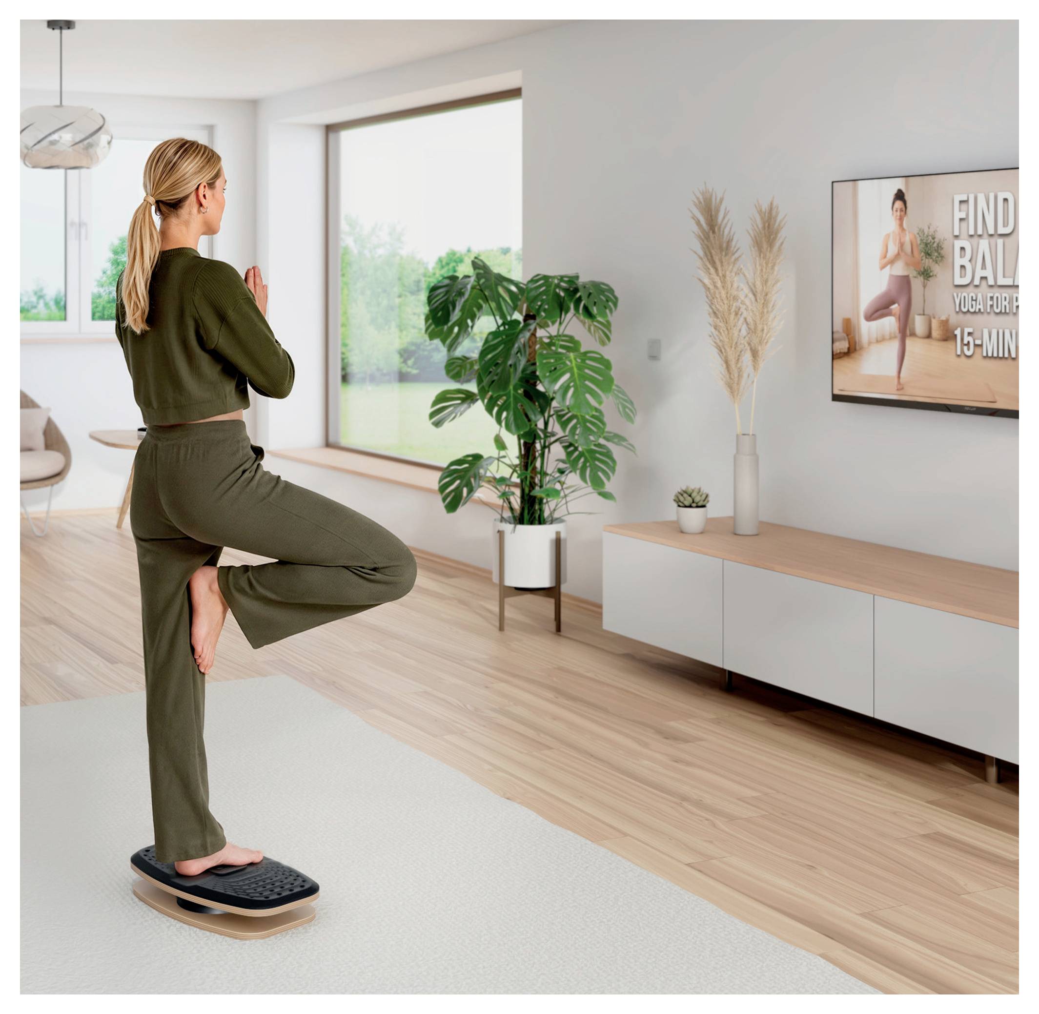 Une femme en équilibre sur une planche oscillante dans la posture de l'arbre lors d'une séance de yoga en intérieur, regardant un entraînement d'équilibre de « 15 MIN » sur un téléviseur mural.