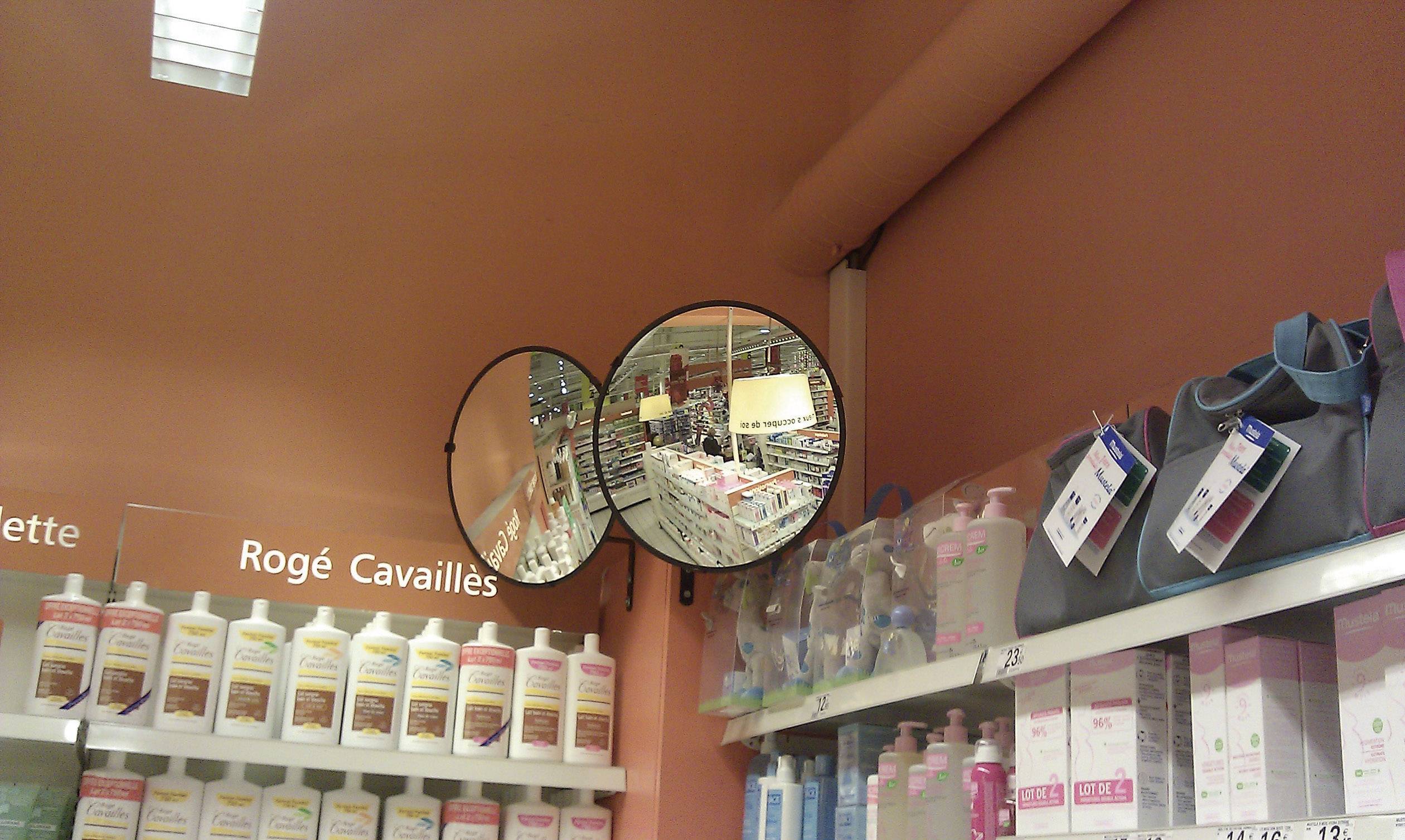 Un intérieur de droguerie montre un miroir reflétant des étagères de produits cosmétiques. À gauche, on distingue des produits de soin corporel.