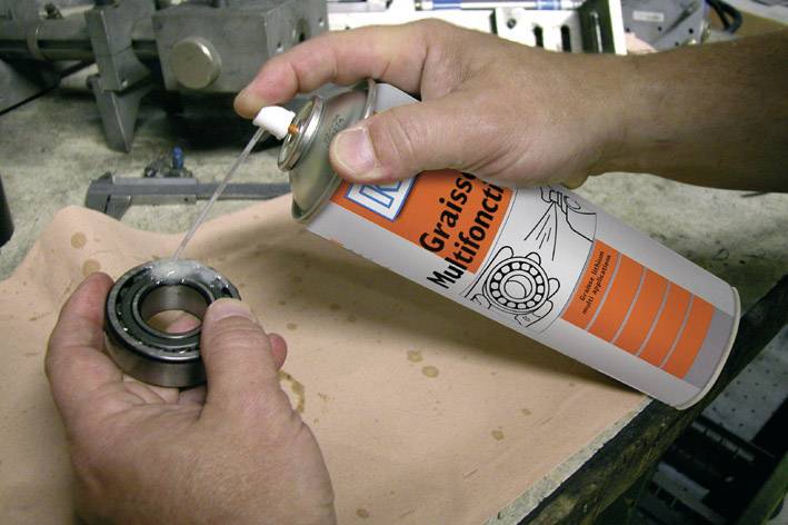 Une personne pulvérise un roulement à billes avec un lubrifiant multifonction à partir d'un aérosol sur une table de travail.