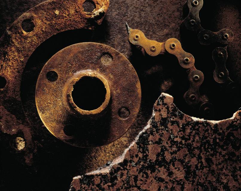 Des pièces métalliques rouillées et des chaînes sont posées sur une surface sombre à côté d'une pierre brisée.