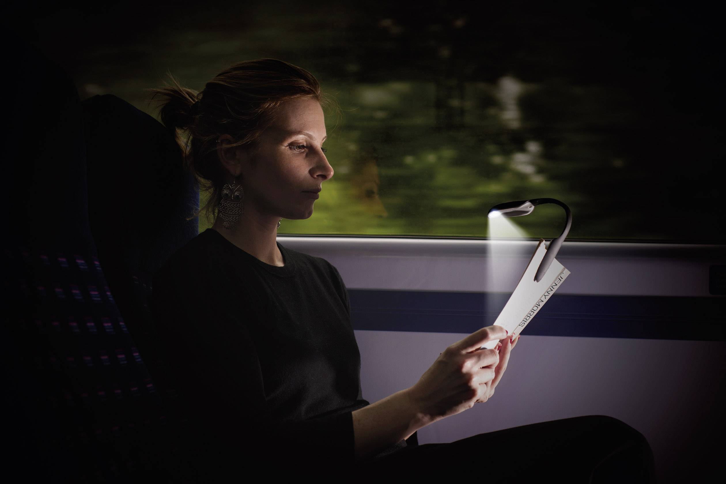 Une personne lit un livre dans un train éclairé au crépuscule. Elle est assise près de la fenêtre, alors que le train est en mouvement.