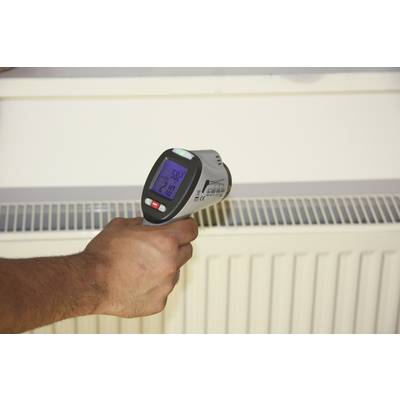 Une main tient un thermomètre infrarouge qui mesure la température d'un radiateur. L'affichage indique 52,3 degrés Celsius.