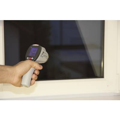Une main tient un thermomètre infrarouge devant une fenêtre, l'écran affiche 26,9 degrés.