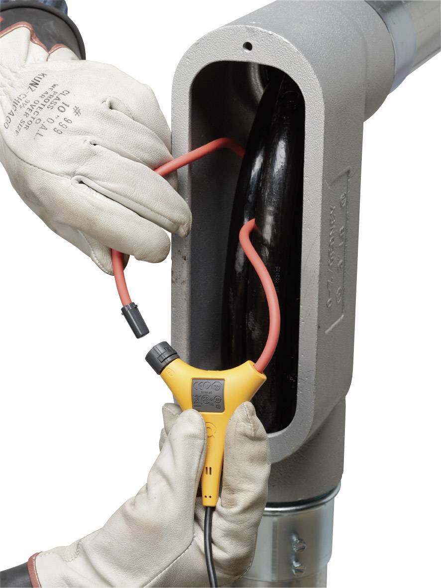 Une personne portant des gants de protection effectue une mesure de câble sur un tuyau gris à l'aide d'un appareil de mesure orange.