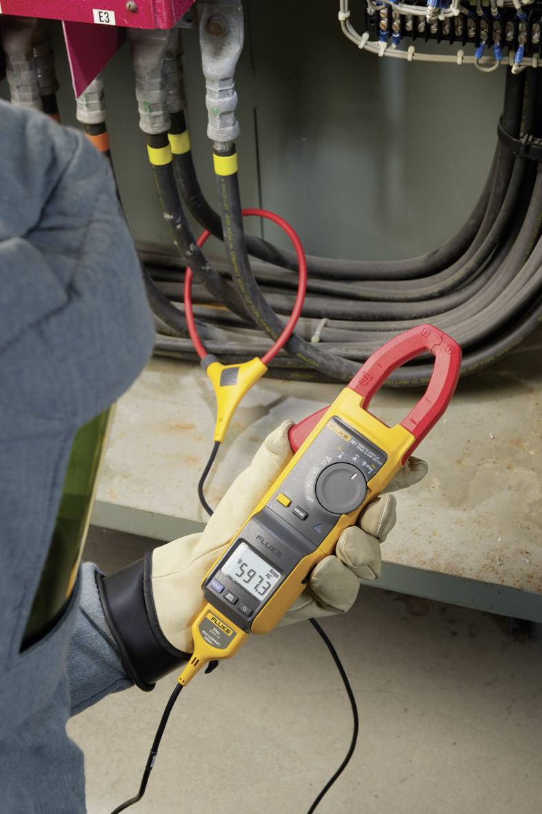 Une personne mesure le courant sur plusieurs câbles dans un armoire électrique à l'aide d'un multimètre jaune. L'affichage indique '591 A'.