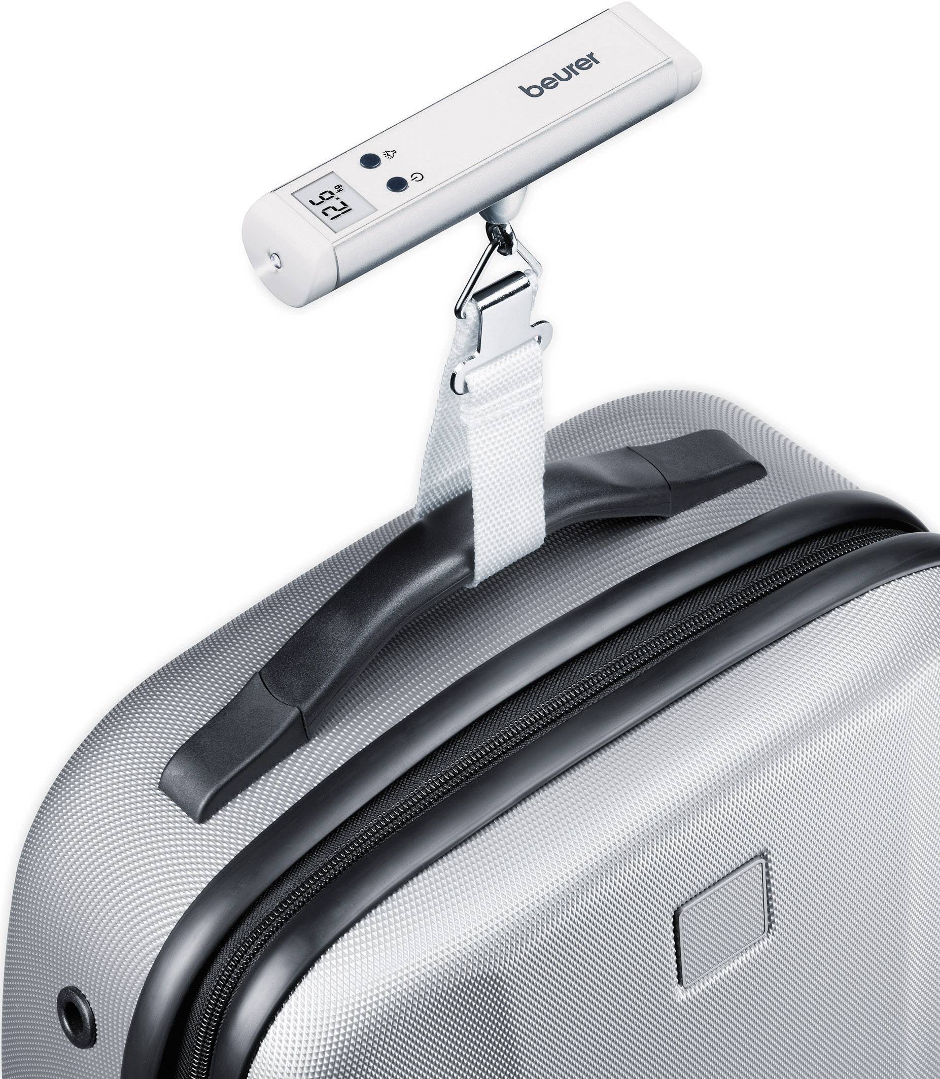 Une balance à bagages indique un poids de 12,5 kg alors qu'elle pèse une valise argentée suspendue à une sangle blanche.