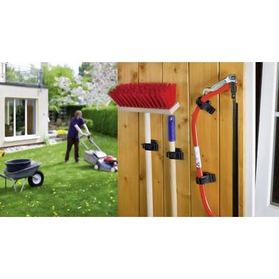 Une personne tond la pelouse dans le jardin. Au premier plan, des outils de jardin comme un balai et une scie sont suspendus à une planche de bois.
