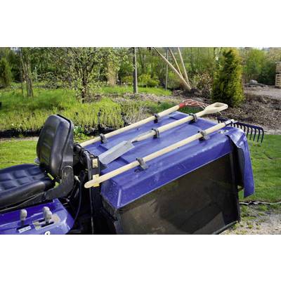 Tracteur tondeuse avec des outils de jardinage suspendus tels qu'une pelle, un râteau et une bêche. À l'arrière-plan, un jardin avec des arbres et des arbustes.