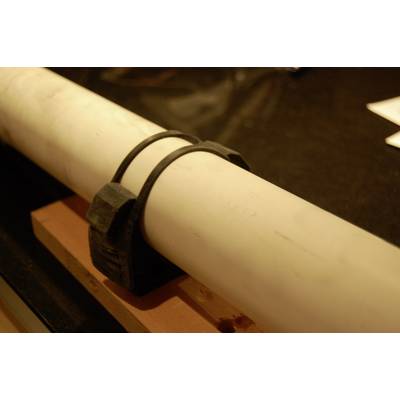 Un tuyau blanc, fixé par un clip en plastique noir, repose sur une poutre en bois.