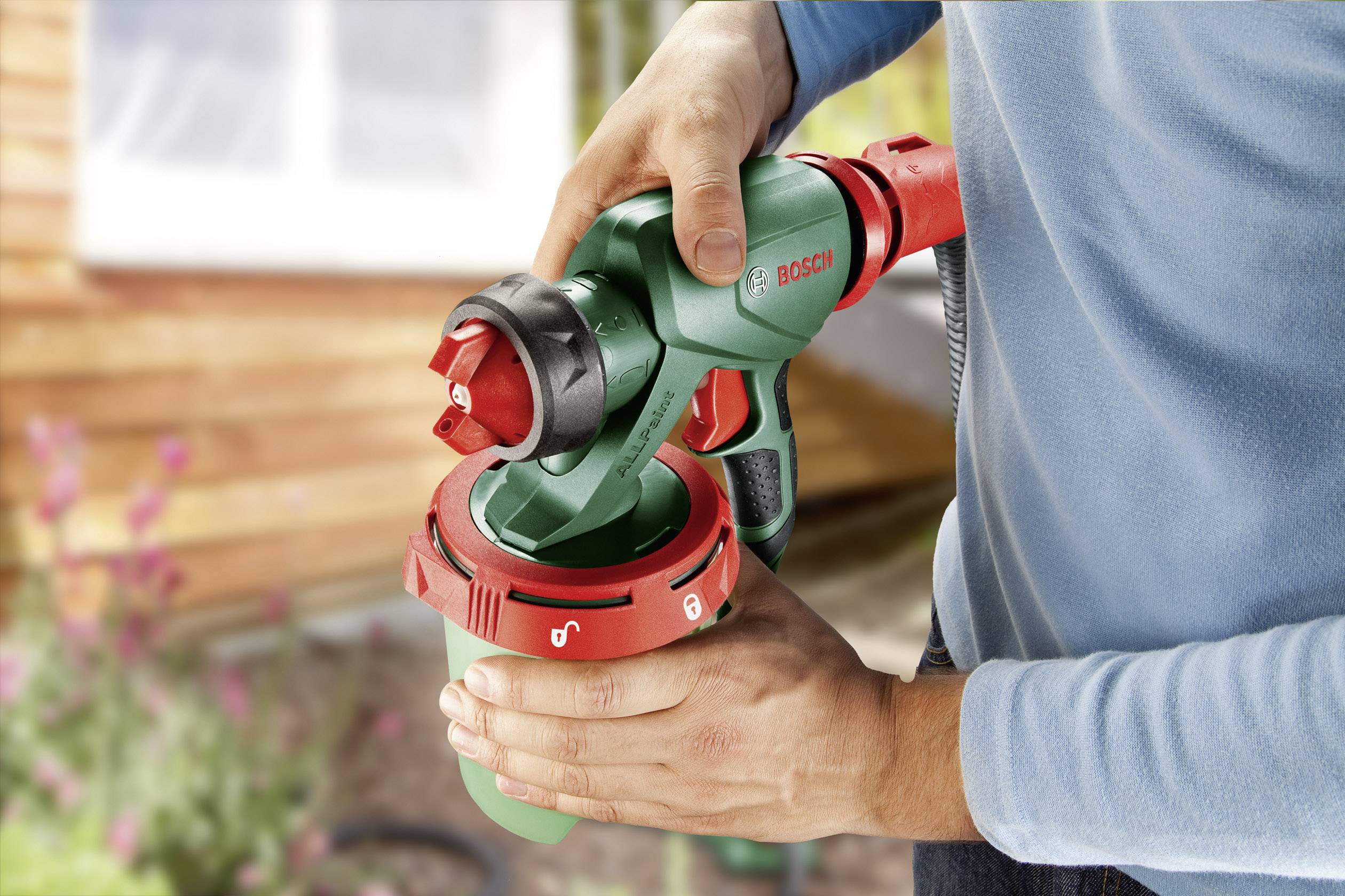 Une personne tient un pistolet pulvérisateur vert et rouge et se prépare à l'utiliser, probablement dans un jardin ou sur une terrasse.