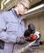 Un homme portant des lunettes de protection et des gants meule du métal avec une meuleuse d'angle dans un atelier. Des étincelles volent de la pièce travaillée.