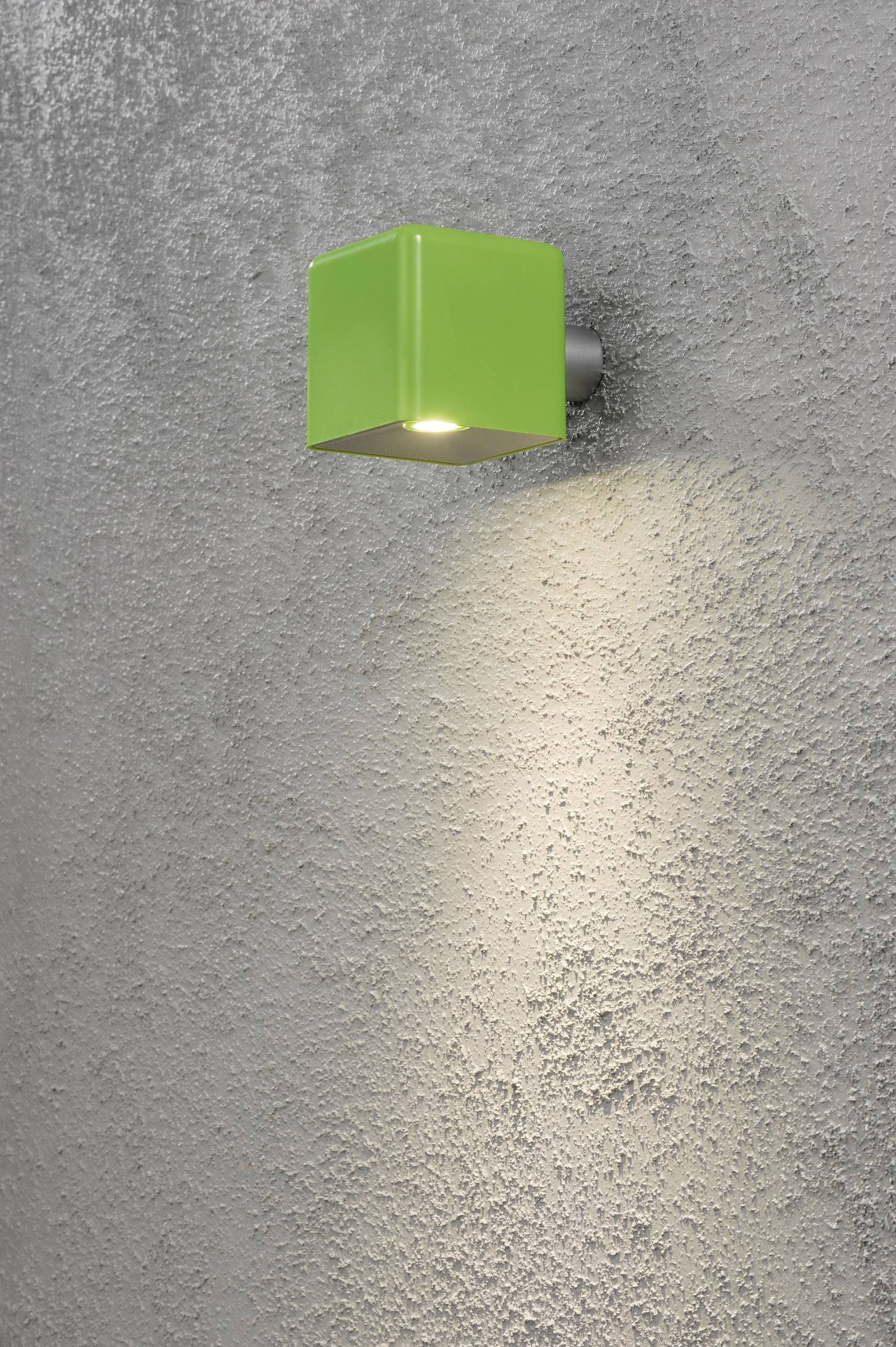 Lampe murale verte en forme de cube illuminant un mur gris à texture rugueuse.