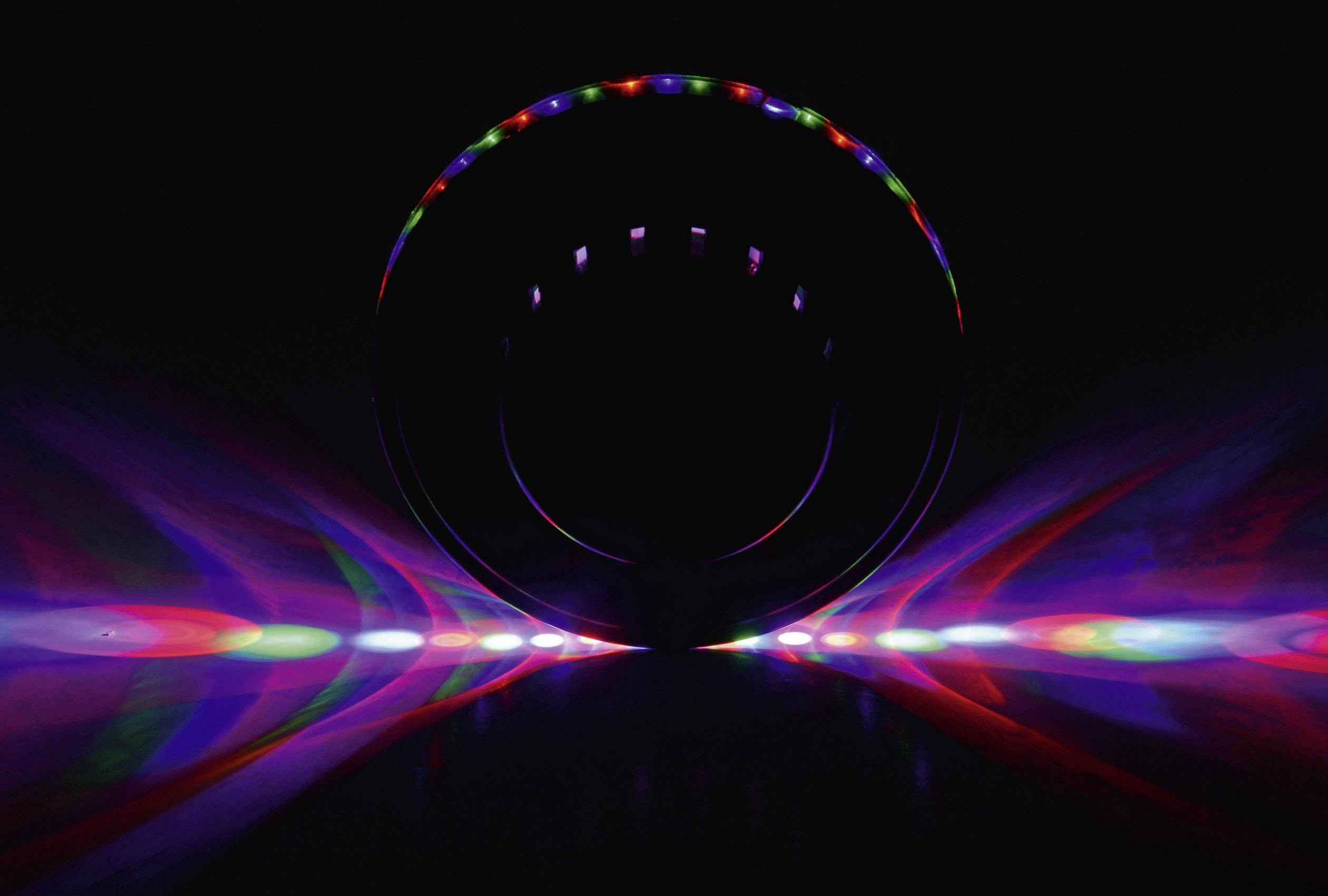 Un objet circulaire génère des motifs lumineux colorés dans un environnement sombre, avec du rouge, du vert et du bleu visibles, présentant des rayons symétriques.