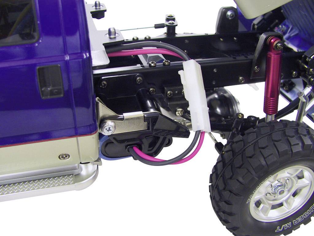 Gros plan d'un véhicule télécommandé. On peut voir des parties de la suspension, des câbles et des pneus. Le véhicule a une carrosserie bleue.