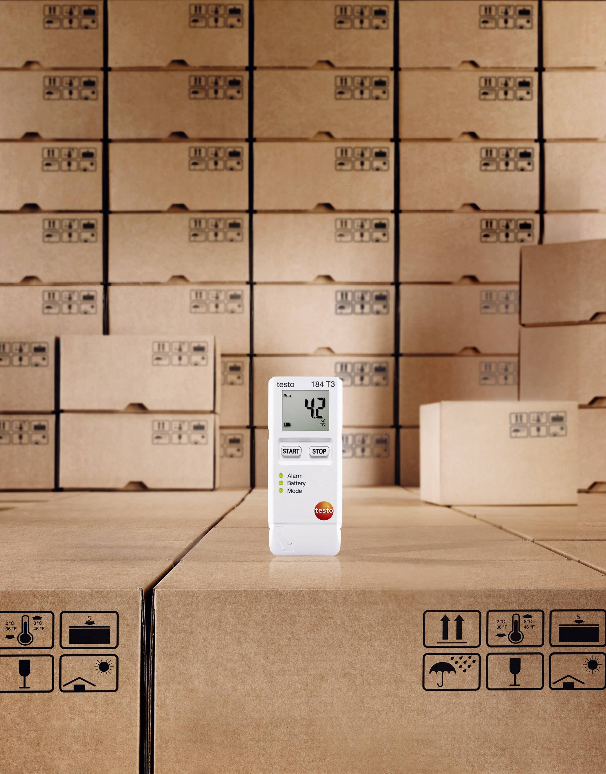 Un indicateur numérique de température et d'humidité affiche '42' sur son écran, entouré de cartons empilés dans un entrepôt.