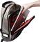 Une main sort un carnet d'un sac à dos gris rempli de stylos et d'appareils électroniques.