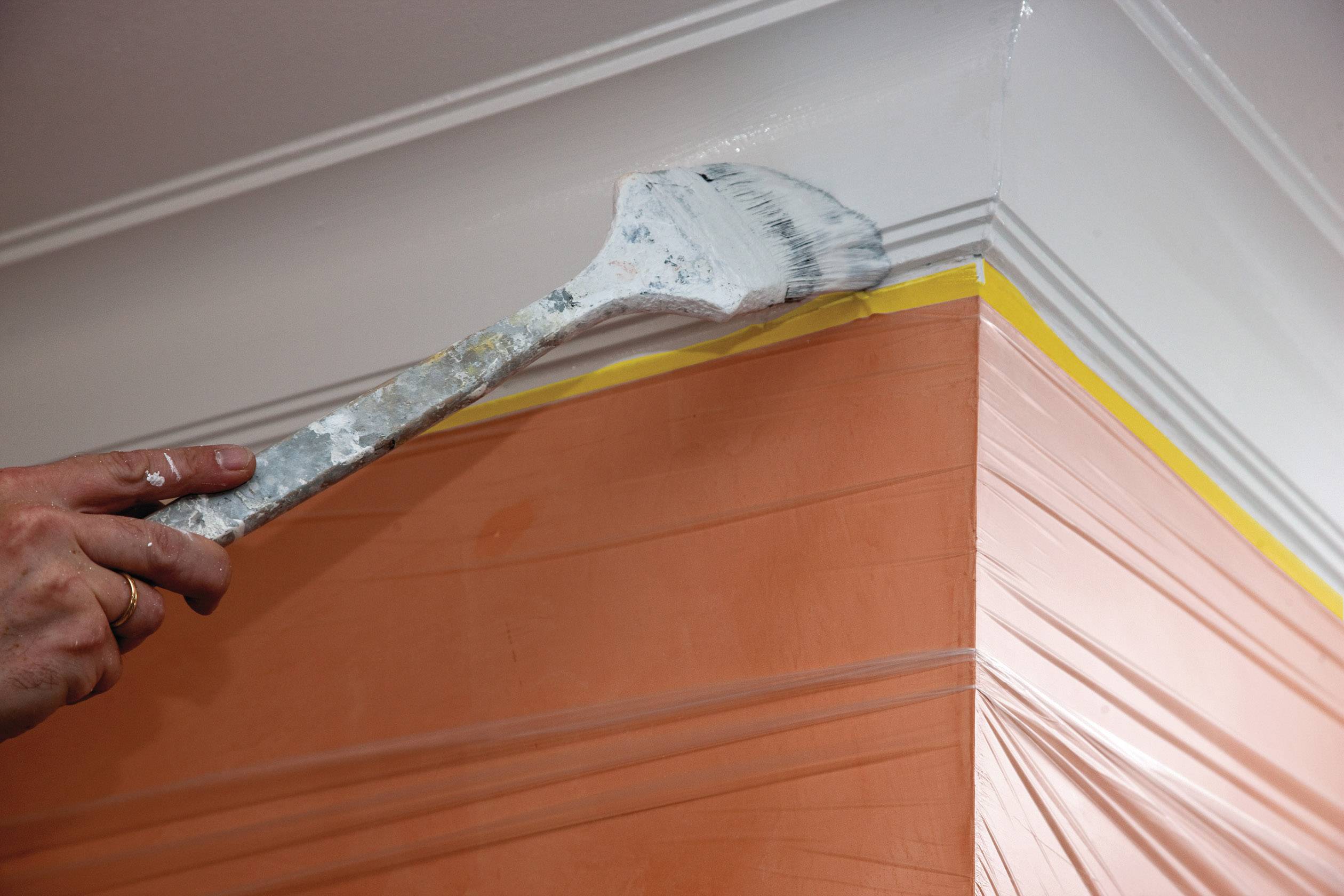 Un pinceau applique de la peinture blanche sur le bord supérieur d'un mur peint en orange. Une ligne jaune sert de repère.