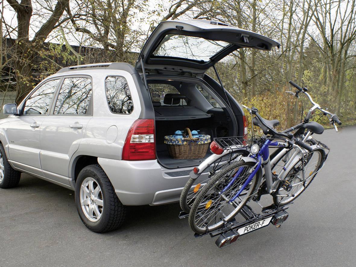 SUV argenté avec le coffre ouvert, rempli d'un panier de pique-nique. À l'arrière, deux vélos sont montés sur un porte-vélos.