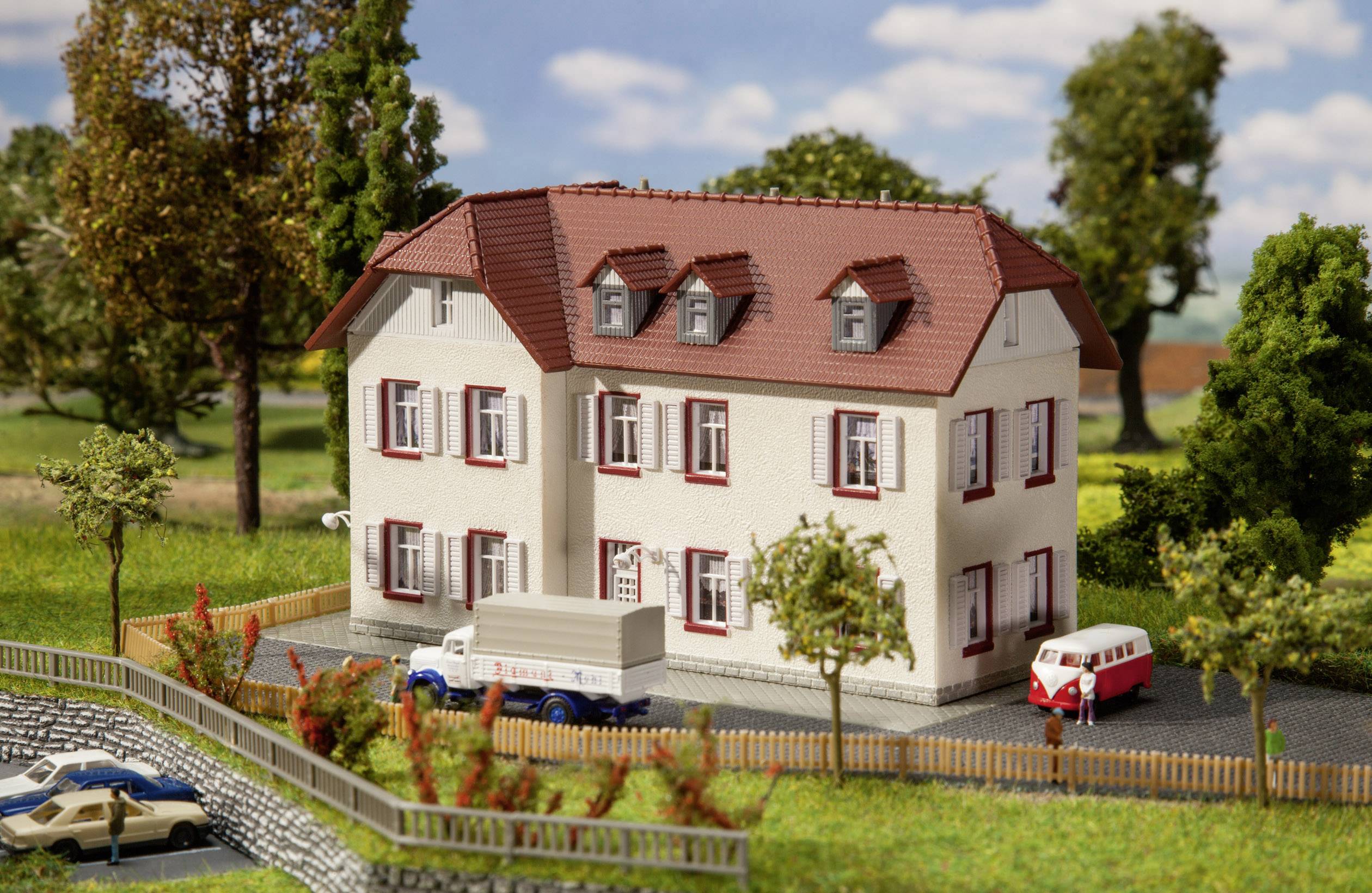 Modèle d'une maison blanche avec un toit rouge et plusieurs fenêtres, entourée d'arbres et de voitures, dans un environnement rural.