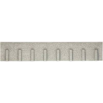 Un mur de briques gris avec des supports verticaux à intervalles réguliers. La surface paraît rugueuse et structurée.
