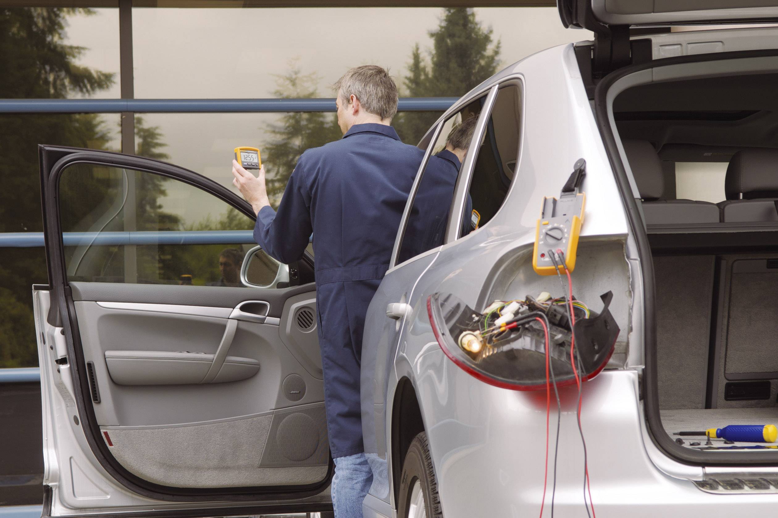 Un mécanicien en bleu de travail vérifie l'électronique d'une voiture argentée à l'aide d'un appareil dans un atelier.