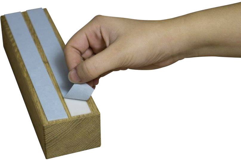 Une main retire une bande de note autocollante bleue d'un bloc en bois comportant plusieurs bandes.