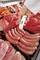 Une main tient un thermomètre dans des saucisses pour en mesurer la température, sur un fond de différents types de viandes fraîches.